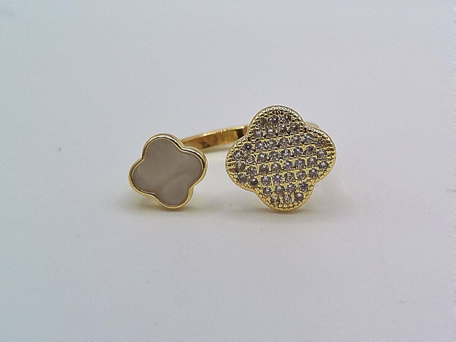 Gold open band ring with a white enamel clover on one end and a crystal-encrusted clover on the other.