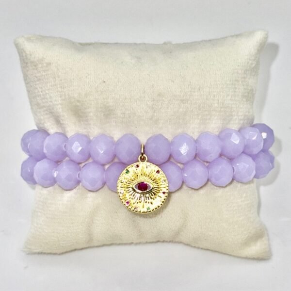 The Occhio Celeste bracelet radiates mystical beauty with faceted lavender crystals that capture light in every movement. At the heart of the bracelet hangs a gold-plated protective eye medallion with a radiant ruby-colored center, symbolizing clarity, intuition, and divine guidance. Whether worn solo for a touch of celestial elegance or stacked for bold expression, this bracelet serves as both a style statement and a talisman of light.