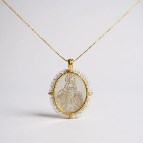 The Ave Maria necklace radiates purity and reverence with its hand-carved depiction of the Virgin Mary, framed in lustrous mother-of-pearl and encircled by a halo of miniature pearls. Crafted in a gold-plated finish, this devotional pendant is both elegant and meaningful, embodying timeless faith and grace. Designed to be cherished close to the heart, it serves as a prayer you can wear every day.