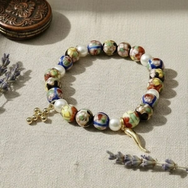 The Fede e Fortuna bracelet captures the essence of Italian tradition and protection. Crafted with hand-painted cloisonné beads in vibrant hues, accented with luminous pearls, and finished with symbolic gold-plated charms — a cross for faith and a cornicello for luck — this bracelet is more than an accessory; it’s a talisman of beauty, meaning, and heritage. Perfect for those who embrace both spiritual strength and good fortune in their journey. Wear it on its own as a statement of faith and fortune, or stack it with the deep red stone beaded bracelet to amplify its bold, passionate energy and create a truly striking layered look.