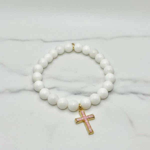 The Rosalina bracelet embodies purity and devotion with timeless elegance. Hand-strung luminous white beads are paired with a gold-plated cross inlaid with radiant pink mother-of-pearl, reflecting light with soft iridescence. A piece that speaks to faith and femininity, it’s as meaningful as it is beautiful. Wear Rosalina alone for a refined statement or stack it with the Luna heart design for a layered expression of love and grace.