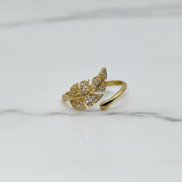 The Foglia Dorata Ring captures the delicate beauty of nature in a fashion-forward design. Crafted in gold-plated brass, this adjustable ring showcases a sparkling pavé crystal leaf that wraps gracefully around your finger. Its open band ensures a comfortable fit while adding a touch of modern sophistication. A perfect piece for layering or wearing solo, this ring embodies effortless glamour and everyday versatility. Whether worn casually or as a statement accessory, the Foglia Dorata Ring is a timeless expression of natural beauty elevated with radiant sparkle.
