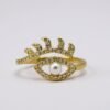 The Occhio di Perla Ring is a striking fusion of symbolism and sophistication. Crafted in luminous gold plating, this captivating design features an eye-shaped silhouette lined with sparkling pavé crystals, crowned by delicate lashes that shimmer with light. At the center rests a radiant pearl, symbolizing wisdom, clarity, and protection. Inspired by the ancient talisman of the “all-seeing eye,” this ring offers both fashion-forward appeal and a touch of spiritual meaning—perfect for those who embrace bold style with intention. Its adjustable band ensures a comfortable fit, making it as versatile as it is stunning. Whether worn as a statement piece or stacked with other Bella Pia favorites, the Occhio di Perla embodies protection, power, and timeless beauty.