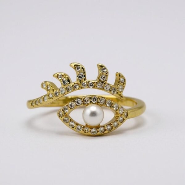 The Occhio di Perla Ring is a striking fusion of symbolism and sophistication. Crafted in luminous gold plating, this captivating design features an eye-shaped silhouette lined with sparkling pavé crystals, crowned by delicate lashes that shimmer with light. At the center rests a radiant pearl, symbolizing wisdom, clarity, and protection. Inspired by the ancient talisman of the “all-seeing eye,” this ring offers both fashion-forward appeal and a touch of spiritual meaning—perfect for those who embrace bold style with intention. Its adjustable band ensures a comfortable fit, making it as versatile as it is stunning. Whether worn as a statement piece or stacked with other Bella Pia favorites, the Occhio di Perla embodies protection, power, and timeless beauty.