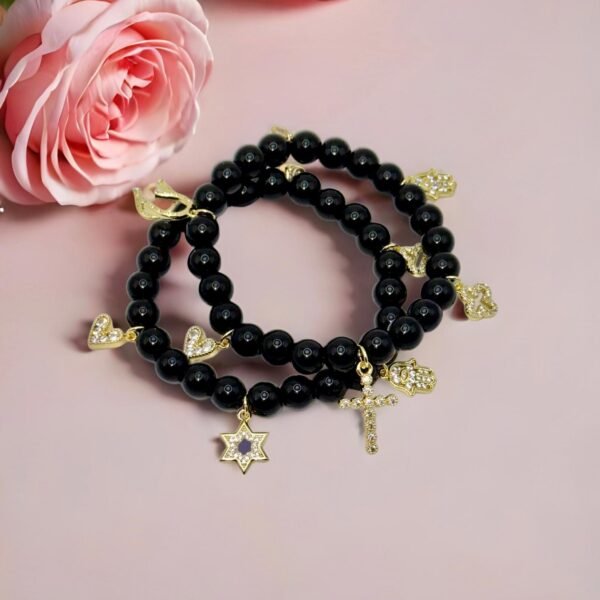 Step into protection and style with the Ginevra’s Amuleto Bracelet, a striking piece crafted with sleek black beads and adorned with radiant gold-plated charms. Featuring meaningful symbols—such as the cross, Star of David, heart, Hamsa hand, clover, and horseshoe—this bracelet celebrates spirituality, luck, and love all in one. Whether worn daily as a personal talisman or styled as a bold fashion statement, Ginevra’s Amuleto Bracelet is designed to keep positivity and elegance close to your wrist. A versatile piece for the woman who embraces both faith and fashion.